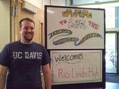 Man wearing a UC Davis shirt next to a welcome Rio Linda High sign